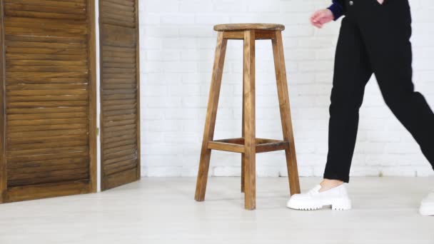 黒いジーンズの女性は 白い靴を示す木製のスツールに来ます ホワイトバックドロップでの靴のプレゼンテーション — ストック動画