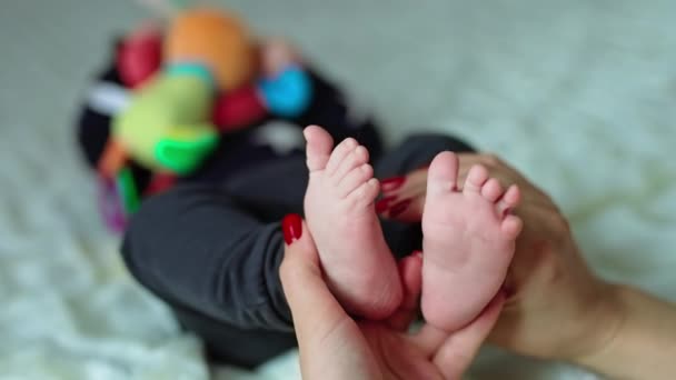 母親は子供の足を握っている 小さな赤ちゃんはつま先を小さく動かして くしゃみを避けます ブラーレッド バックドロップ — ストック動画