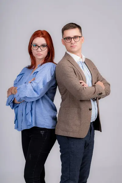 Man and woman in glasses and blue shirt stand back to back with their arms crossed on gray background. The concept of quarrel disagreement conflict of interests.
