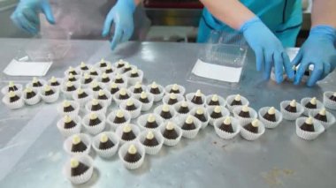 Tek tek ambalajlı güzel şeker konileri masanın üzerinde. Eldivenli işçiler şekerleri plastik kutulara koyarlar..