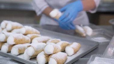 Krem şantili ve pudra şekerli Cannoli tatlısı. Kadın işçi şekerleri plastik pakete koyar. Kapat..