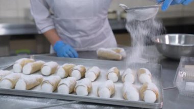 Dekorasyon için metal tepsinin üzerine tuzlu cannoli tatlısı konmuştu. İşçi tatlıları süzgeçten şeker tozuyla kaplıyor. Kapat..