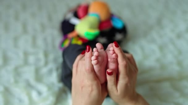 母亲接过她儿子的小脚 拍了拍 小男孩抱着一个明亮的玩具躺在床上 模糊的背景 — 图库视频影像