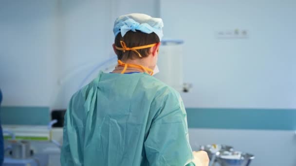 为手术做准备的男性外科医生背对着摄像机站立着 售货员把这个巨大的现代器械拖进手术室 — 图库视频影像