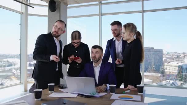 ビジネスマンは従業員に囲まれたコンピュータに座っている チームメイトがアイデアを共有し 最良の結果を伝える — ストック動画