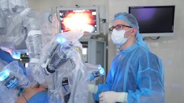 4つのロボットアームが患者の腹に入っています 外科医は装置を握り モニターのプロセスを監視します — ストック動画