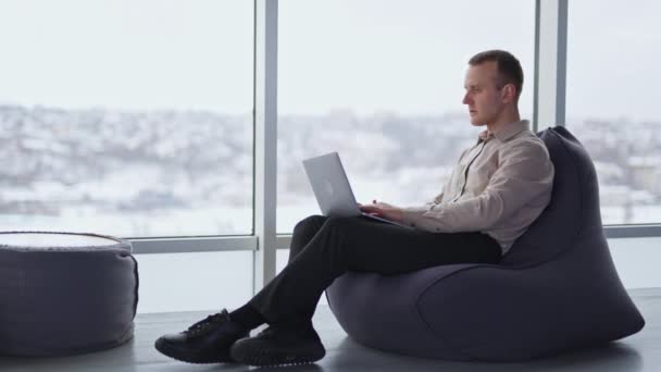 남자는 의자에 노트북에서 합니다 파노라마 창이있는 방에서 편안한 분위기 — 비디오