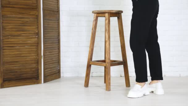 白い巨大な靴を示す黒いジーンズのモデル 女性はファッショナブルな履物を見せるために回ります バックドロップの木製のタブレット — ストック動画