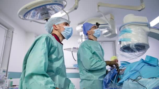 手術に従うために スクリーン上で意図的にまっすぐに見ている男性の医師 仕事中の医療チームの低角度ビュー — ストック動画