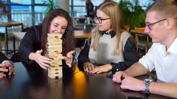 快乐快乐的一群年轻人玩棋盘游戏 长卷发的女人从塔上拖砖头 其他人看着她 — 图库视频影像
