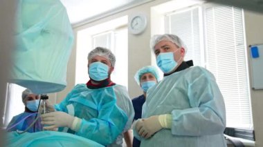 Maskeli iki cerrah hastayı ameliyat edip süreci tartışıyor. Doktor karmaşık aracı hastanın üzerine uygula.