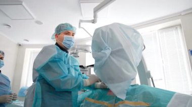 Orta yaşlı doktor enstrümanı dikkatlice hastanın vücuduna sokuyor. Odaklanmış cerrah, hemşire ve anestezi uzmanı ekranı izleyin..