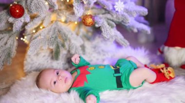 Yeşil elf takım elbiseli beyaz çocuk yeni yıl ağacının altında yatıyor. Yeni doğan çocuk Noel süslemelerinde.