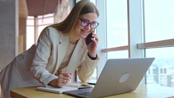 Neşeli Uzun Saçlı Gözlüklü Kadın Telefonda Masanın Üzerinde Eğik Duruyor — Stok video