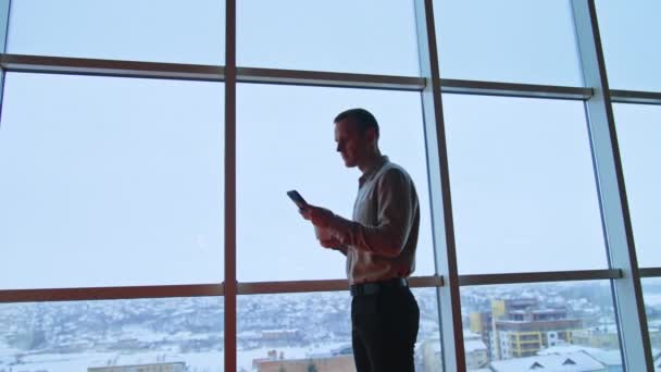 Спокійний Серйозний Чоловік Стоїть Біля Панорамного Вікна Тримаючи Чашку Телефон — стокове відео