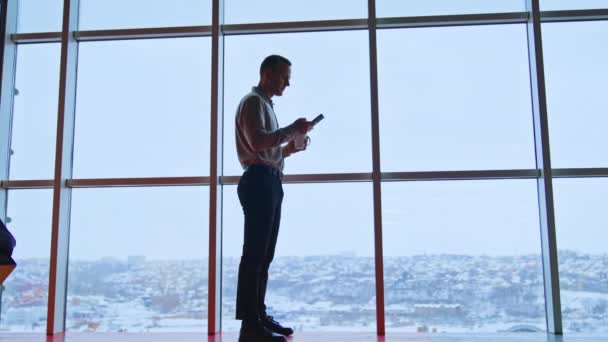 Молодий Чоловік Стоїть Високо Біля Панорамного Вікна Чашкою Телефоном Руках — стокове відео