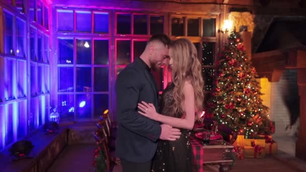 穿着漂亮衣服的男人和女人在乡间别墅里约会 在装饰过的桌子和圣诞树前拥抱亲吻的情侣 — 图库视频影像