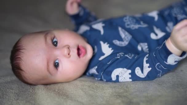 Uśmiechnięty Chłopiec Niebieskich Ubraniach Dinozaurami Leży Plecach Szare Oczy Słodkie — Wideo stockowe