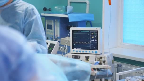 手術中の患者の生命の徴候を有する小さな黒いスクリーン 手術でそれらを使用するために上昇力の青い帽子の外科医 — ストック動画