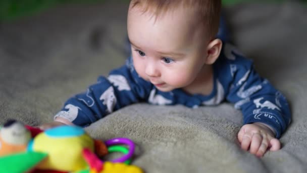 可爱的男孩躺在床上看着面前的玩具 有兴趣的婴儿摸着明亮的玩具 模糊的背景 — 图库视频影像
