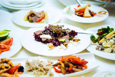 Beyaz tabakta çeşitli salatalar ve etler.