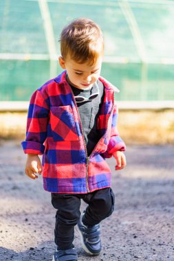 Sevimli küçük çocuk kırmızı ve siyah ekose ceketli yolda yürüyor.