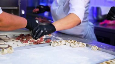 Mutfakta işbirliği yapan üç aşçı et mantısı üretiyor. İşçiler pelmeni üretmenin farklı aşamalarında sorumluluk yayarlar..