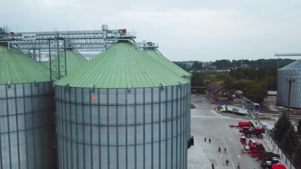 近くに多様な農業機械を備えたエレベーターの金属製タンク 人々は巨大な銀製のシスターを歩いています 上からの眺め — ストック動画