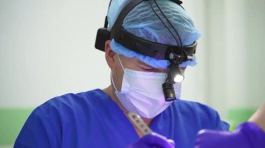 Hastayı ameliyat ederken kafasına cihaz takan orta yaşlı bir doktor. İşine odaklanmış bir cerrahın yakın portresi..