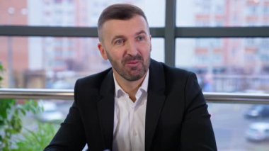 Orta yaşlı, iyi görünümlü iş adamı, çalışanlarıyla fikirlerini dinleyerek konuşuyor. Genç, uzun saçlı bayan ofis çalışanı patronuna cevap veriyor..
