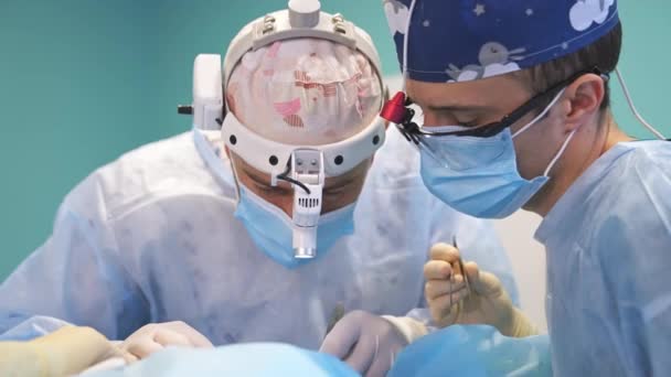 Два Хирурга Масках Устройствах Головах Склонились Над Пациентом Врачи Выполняют — стоковое видео