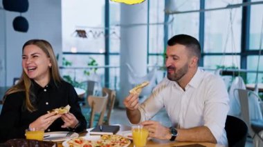 Meslektaşlar kafede pizza yiyorlar. Kadın ve erkek masada oturup yemeğin tadını çıkarıyorlar. İnsanlar konuşup gülüyor..