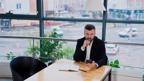 Προσεκτικός Επιχειρηματίας Που Κάθεται Στο Τραπέζι Κρατώντας Τηλέφωνο Στο Χέρι — Αρχείο Βίντεο