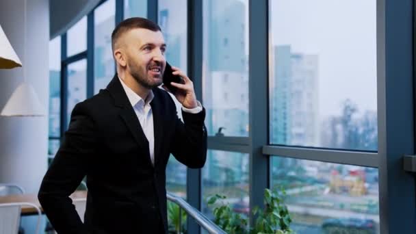 Obchodník Obleku Mluví Telefonu Vesele Stojí Velkého Okna Kanceláři Muž — Stock video