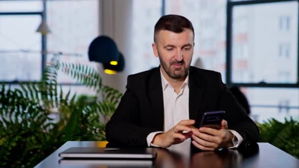 Spokojny Uśmiechnięty Mężczyzna Siedzący Przy Stole Patrzący Telefon Biznesmen Pisze — Wideo stockowe