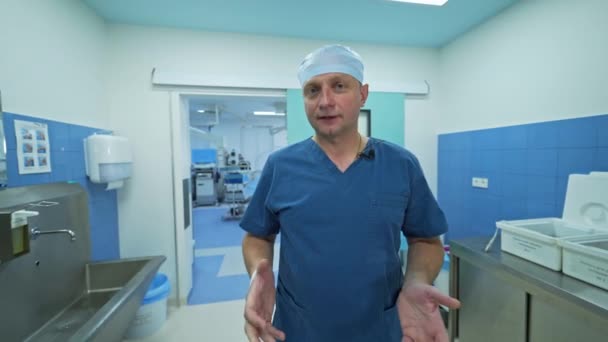 真剣な男性外科医は 手術後にカメラに話しかける 医師は手術劇場の近くのホールに立って手術をコメント — ストック動画
