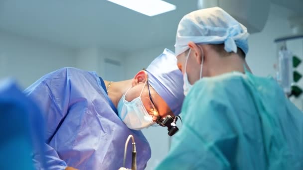 デバイスメガネの中年の男性外科医は 患者の上に非常に低く曲がった 道具や煙を使ったスペシャリストが立ち上がります 男性用医薬品アシスト — ストック動画