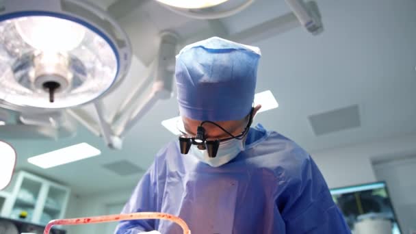 의사의 상부는 구부러졌습니다 안경을 착용한 외과의사는 기구를 조심스럽게 움직입니다 — 비디오