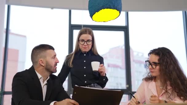 スーツを着た男が座ってフォルダを保持する 女性同僚がコーヒーを飲み ボスと話す — ストック動画