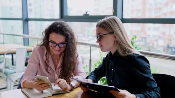 Duas Jovens Mulheres Olham Para Smartphone Discutem Algo Sorrindo Trabalhadoras — Vídeo de Stock