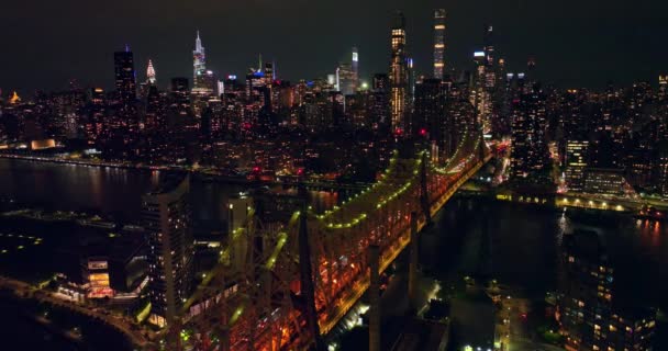 コック クイーンズボロ ブリッジは夜に素晴らしいバックライトを浴びせています 明るく輝くニューヨークの高層ビルの素晴らしいパノラマ — ストック動画
