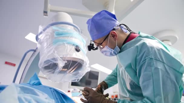 外科医は患者の上に曲がっている 医学の専門家は患者を縫うのに金属用具を使用します — ストック動画