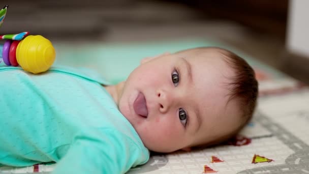 カメラを見ている美しい灰色の目を持つ甘い赤ちゃんの顔 いい子が舌を出してゆっくり動きます クローズアップ — ストック動画