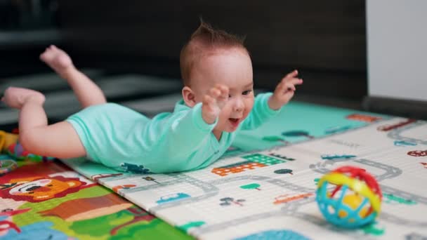 身穿蓝色衣服的活泼婴儿躺在彩色垫子上 有趣的孩子很高兴看到他面前有一个玩具 — 图库视频影像