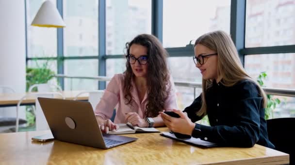 若い女性の同僚は ラップトップの前に座って それを見て 笑っている 共同作業者がアイデアを共有し 新しいものを作る — ストック動画