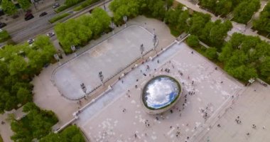 İnsanlar Chicago 'da ünlü Cloud Gate heykelinin etrafında dolanıyor. Fasulye gökyüzünü, bulutları, parkı ve gökdelenleri yansıtıyor. Üst görünüm.