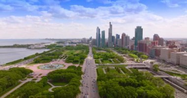Yeşil park bölgesinden çok sayıda aracın geçtiği geniş bir yol. Chicago şehir manzarası ve gökdelenler arka planda.
