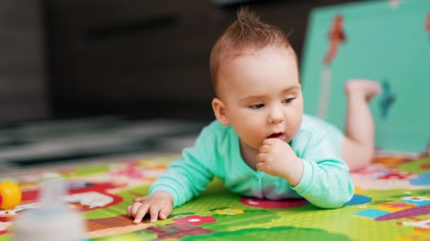 可爱的男婴 一头可笑的头发躺在垫子上 可爱的幼儿对玩具感兴趣 靠近点 — 图库视频影像