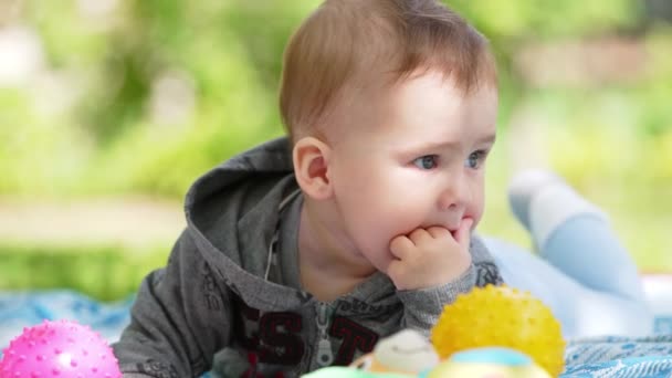 かわいい落ち着いた深刻な赤ん坊の少年は草の上に休んでいる 甘い小さな子供が口に手を引いている クローズアップ — ストック動画