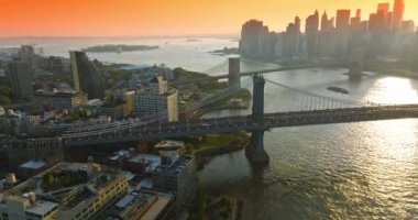 Manhattan ve Brooklyn Köprüleri, East River üzerinde. New York gökdelenlerinin siluetleri turuncu gökyüzünün arka planında.